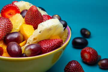 Uma porção de frutas dentro de uma vasilha amarela com fundo na cor azul tiffany.