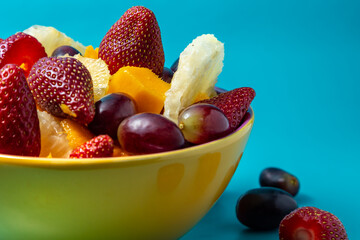 Uma porção de frutas dentro de uma vasilha amarela com fundo na cor azul tiffany.
