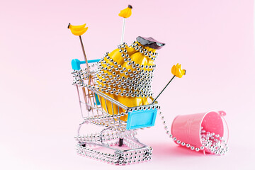 Shopping trolley with silver Christmas beads on a pink background. Shopping cart with creative Christmas gifts. Christmas decoration concept