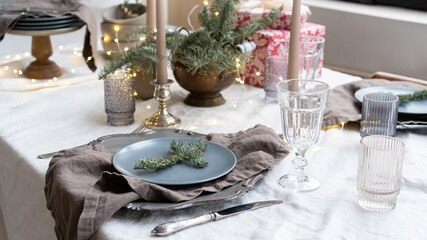 Christmas table setting. Spruce twigs as a Christmas decor in the restaurant. Linen tablecloth and napkins on the table. Minimalistic style in the interior design. Elegantly set Christmas dinner table