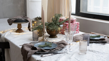 Christmas decor in the interior of the restaurant. A table set for Christmas dinner with fir tree twigs, glasses, candles and gift boxes. Rustic style in the interior of the kitchen and dinning room.