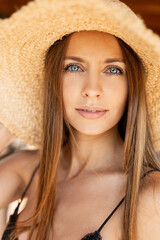 Summer portrait of a beautiful girl with a pretty model face and amazing blue eyes in a woven straw hat on the street, close-up