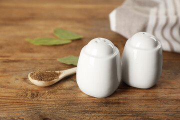 White ceramic salt and pepper shakers with spoon on wooden table, closeup