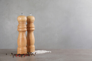 Wooden salt and pepper shakers on grey table, space for text. Spice mill - obrazy, fototapety, plakaty