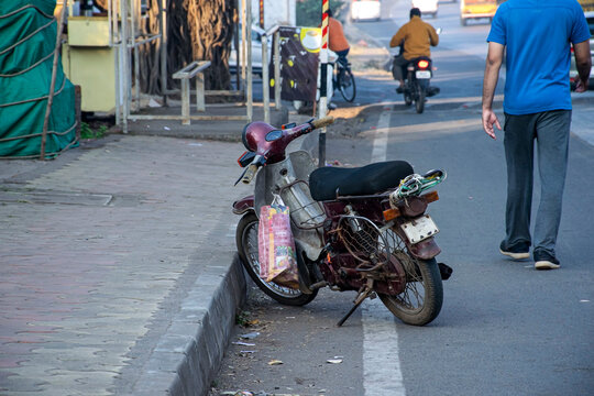 Stock photo of maroon color M80 motorbike parked near sidewalk or footpath, people roaming on road ,motorbike moving forward at Kolhapur,Maharashtra,India.