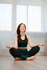 Young athlete sitting in the lotus position is sitting on the floor in an apartment. Concept relaxation and yoga.