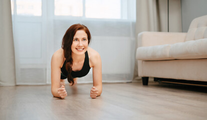 Fototapeta na wymiar Young woman is engaged in fitness at home doing a plank exercise. Concept of sports.