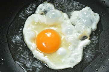fried egg pour from cup for cooking in hot oil on electric pan