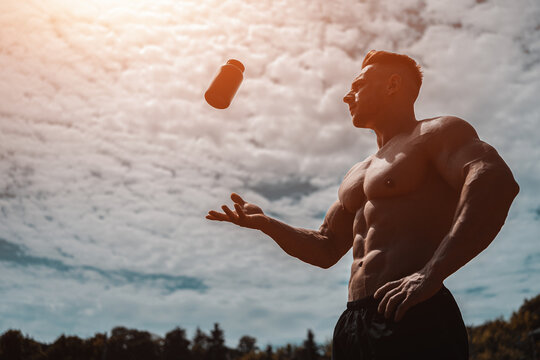 muscular athlete man throw up black container with protein whey powder outdoor