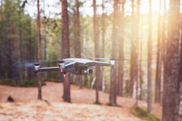 Modern Drone with camera flying in the forest.