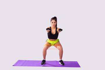 The young woman goes in for sports using sport fitness rubber bands attached to the knees with arms outstretched forward.