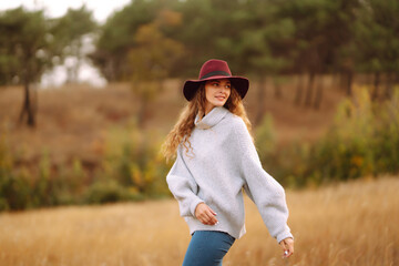 Young woman in sweater and hat enjoys a Autumn day outdoors in a park. Fashion, style concept.