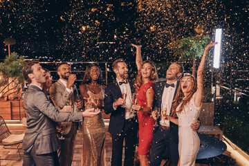 Group of happy people in formalwear having fun together with confetti flying all around
