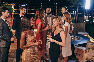 Group of beautiful young people in formalwear communicating and smiling while spending time on luxury party - obrazy, fototapety, plakaty