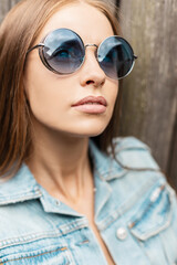 Fashion portrait of beautiful woman with caucasian face in fashionable round sunglasses with vintage jeans jacket outdoors