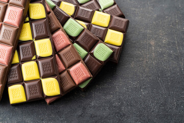 Multicolored fruit chocolate bars on black background. Handmade chocolate with mint, mango, orange, strawberry flavor. Healthy food concept, delicious chocolate sweets for kids, diet, sugar