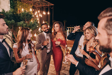 Group of beautiful young people in formalwear communicating and smiling while spending time on luxury party