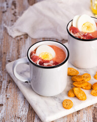 Spanish salmorejo cream soup with ham and egg on a wooden rustic table. Mugs of spicy tomato cold soup