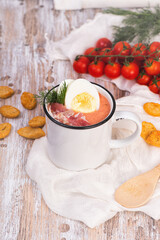 Spanish salmorejo cream soup with ham and egg on a wooden rustic table. Mugs of spicy tomato cold soup