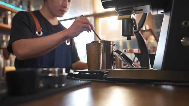 Asian man barista using coffee grinder machine grinding roasted coffee beans at cafe. Male coffee shop owner brewing black coffee serving to customer. Small business restaurant food and drink concept