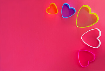 Multi-colored heart shaped cookie cutters over a pink background.