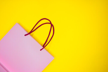 Pink paper shopping bag on yellow background. Black Friday sale shopping.
