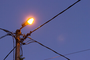 City lantern with wires shines in the twilight night sky
