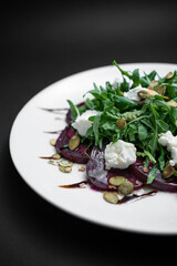 salad with beet, arugula and feta cheese on white plate on black background