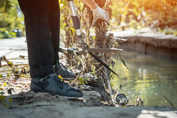 male hands cut branch with garden scissors near river or cleaning city park