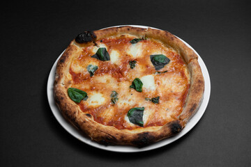 closeup of margarita pizza with tomatoes, cheese and basil on black background