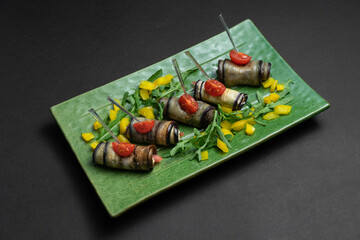 close up of eggplant rolls with cream cheese on green plate on black background