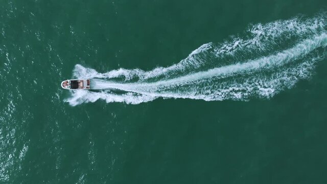 Motorboat sailing in the turquoise sea. Aerial footage. Speed boat sailing in the calm sea making foamy waves. Top view during the daytime in Benidorm, Spain. Vacations and travel concept.