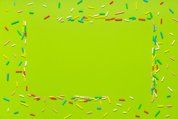trendy frame of colorful sprinkles over green background, decoration for holiday