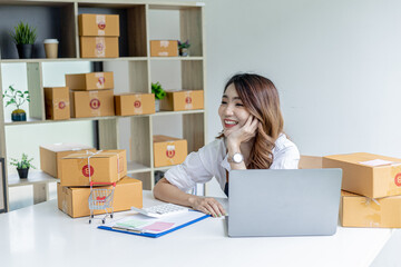 An Asian woman with a happy smile on her face after closing sales targets, she owns an online store, she packs and ships through a private shipping company. Online selling and online shopping concepts