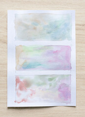 Abstract watercolor stains background on white paper sheet with wood background.