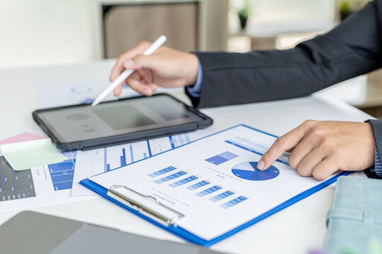 Businessman is using tablet to compare information on financial documents, he is checking company financial documents in office, company financial statements. Concept of financial management.
