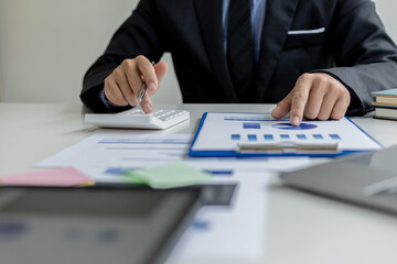 Close-up of a business man using a white calculator, a financial businessman examining the numerical data on a company financial document, He uses a calculator to verify the accuracy of numbers.