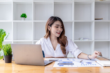 A beautiful Asian woman sits in her office, an Asian businesswoman checking the financial documents of a company she and her partner set up. Concept of company financial management.