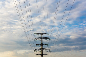 Electric high-voltage poles stand against the background of blue sky and clouds.