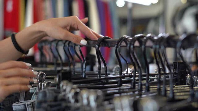Close up of woman's hands choosing denim pants, clothes in a store, searching or buying cheap clothes on a hanger at a flea market.