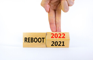2022 reboot new year symbol. Businessman turns a wooden cube and changes words 'Reboot 2021' to...