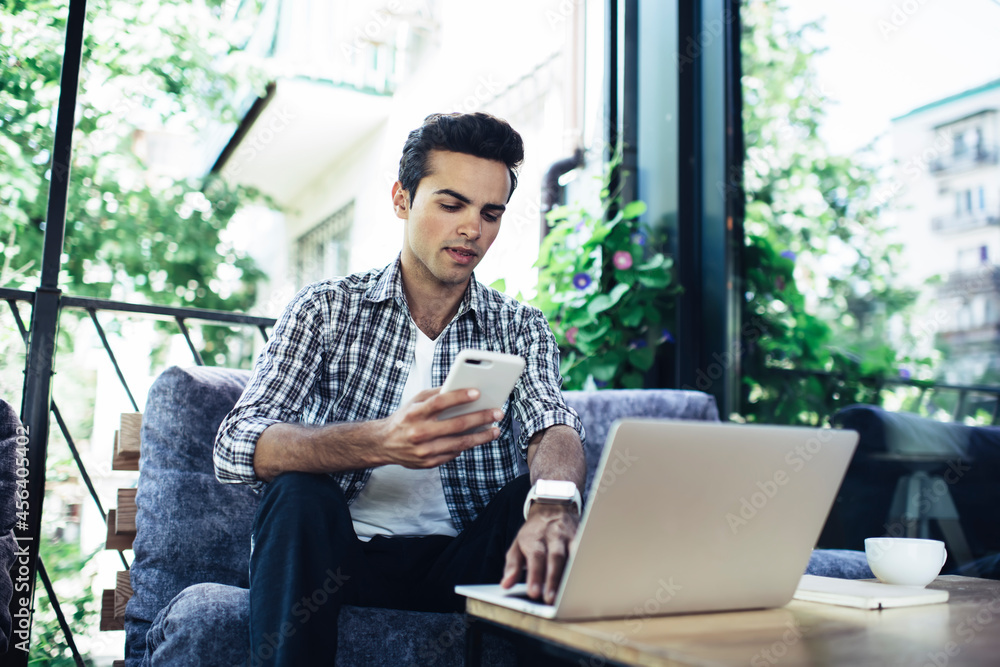 Poster caucasian freelance copywriter using smartphone and laptop for sharing media files via bluetooth con