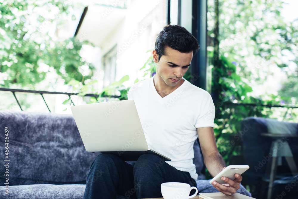 Poster millennial male generation z with netbook computer using modern cellphone device for making online b