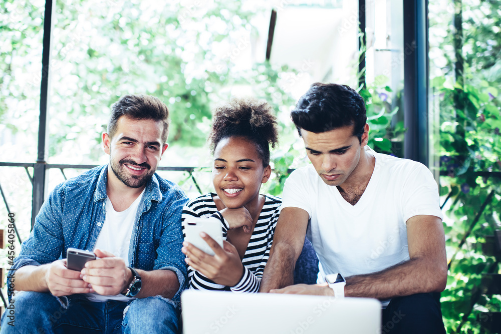 Poster portrait of cheerful male blogger with mobile device for sharing media files smiling at camera durin