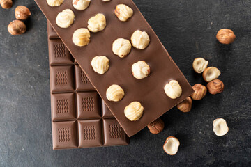 Milk chocolate bar with whole hazelnut kernels on a black background. Healthy food concept, delicious chocolate sweets for kids, diet, sugar