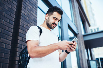 Young male travel blogger browsing website on cellphone device using 4g wireless for checking GPS on location application, millennial hipster guy reading received message during mobile mailing