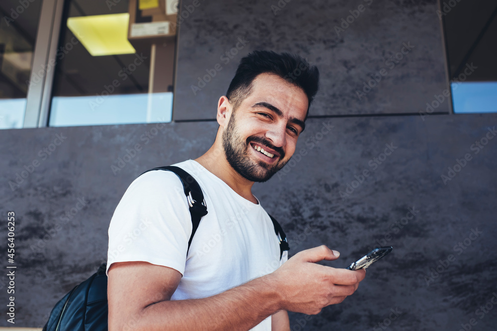 Poster half length portrait of cheerful travel blogger in casual wear smiling at camera while messaging in 