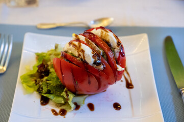 Big red french tomato served with fresh mozzarella cheese, basil pesto and creme balsamico as starter in restaurant in Provence, France