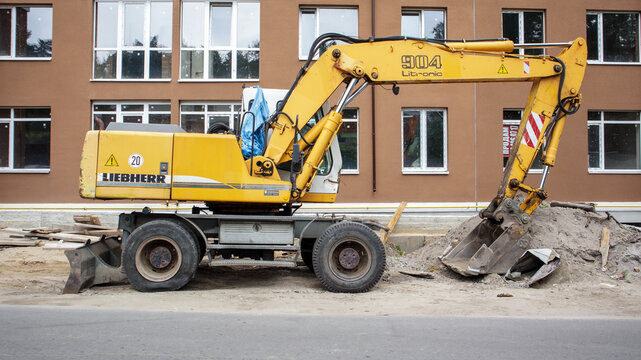 Mobile crane loader of yellow color on the background of a building under construction. International hardware manufacturer. The excavator is used for earthworks. Ukraine, Kiev - September 11, 2021.