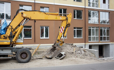 Mobile crane loader of yellow color on the background of a building under construction. German-Swiss international equipment manufacturer. The excavator is used for earthworks.